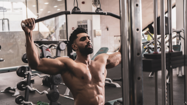 A person performs lat pulldowns without a shirt on.