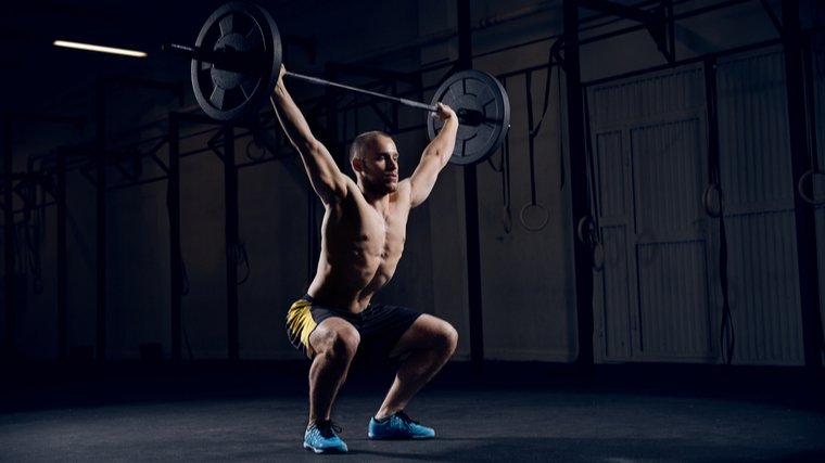 A person catches the barbell in a snatch in the gym.