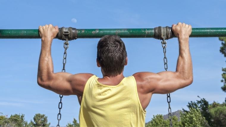 man in tank top performing a pull-up on a swing 