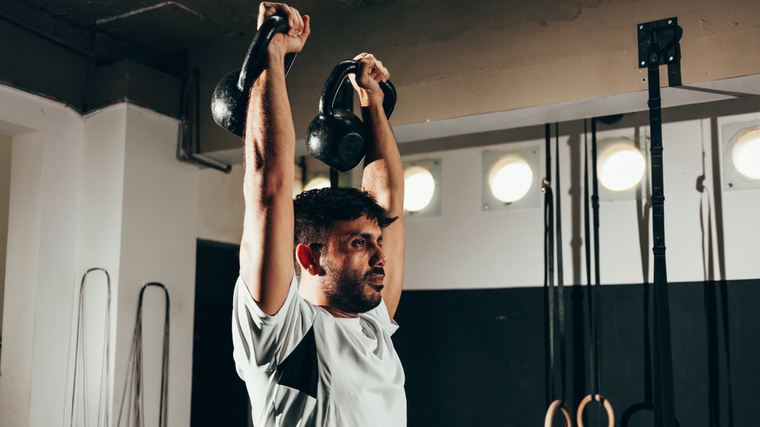 A person performs a double overhead kettlebell press in the gym.