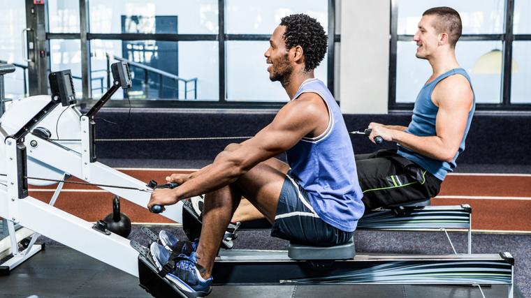 Two people use a rower in the gym.