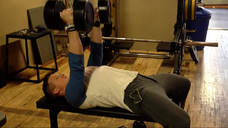 A person holds dumbbells above him on a bench.