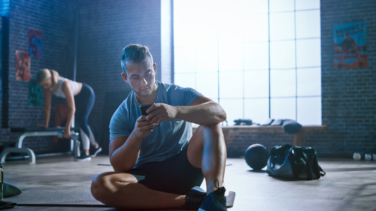 A person sits on the ground in the gym while looking at their smartphone.