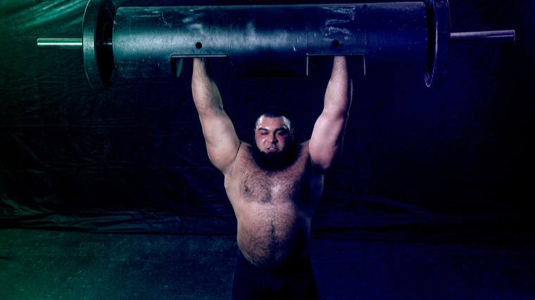 A shirtless, bearded person performs a log press.