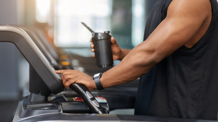 A cropped image shows the arms of a person preparing to run on a treadmill while holding a shake.