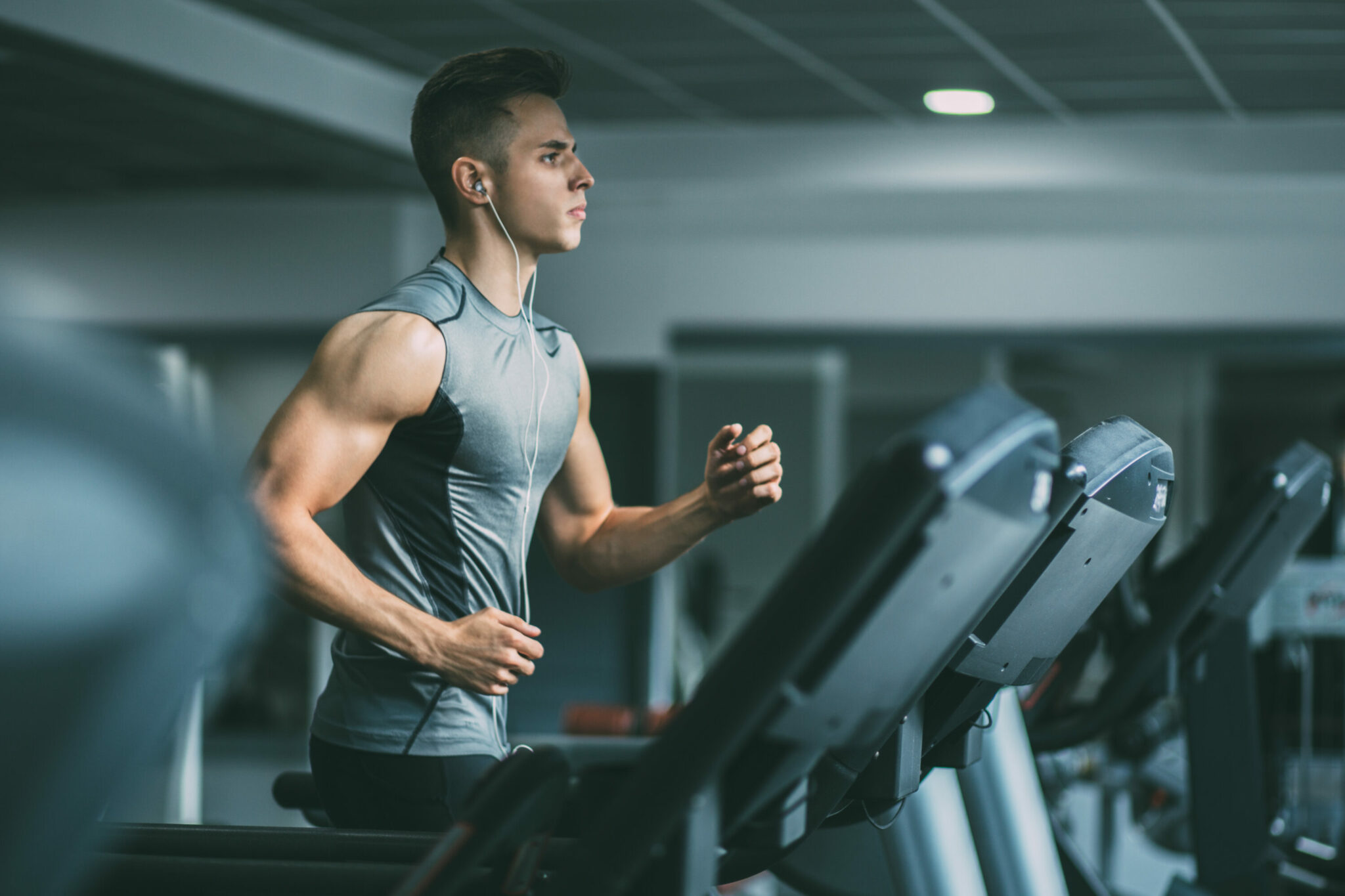 A person wearing a grey compression tank top runs on a treadmill.