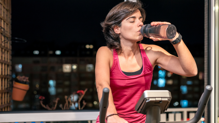 A person drinks water while using an elliptical.