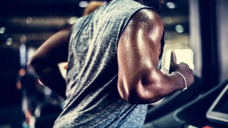 A close up of a person's arm and torso shows them sweating while running on a treadmill.