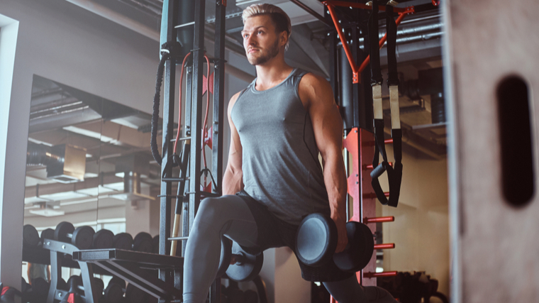 A person wearing a tank top, leggings, and shorts performs dumbbell lunges in the gym.