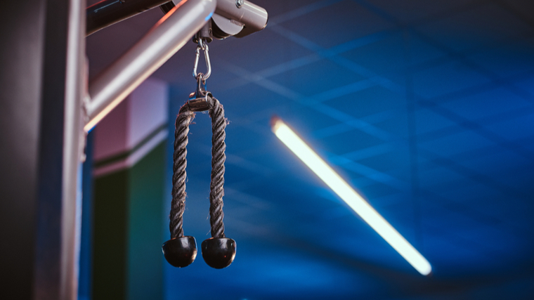 A triceps rope hands suspended from a cable machine against a blue ceiling background.