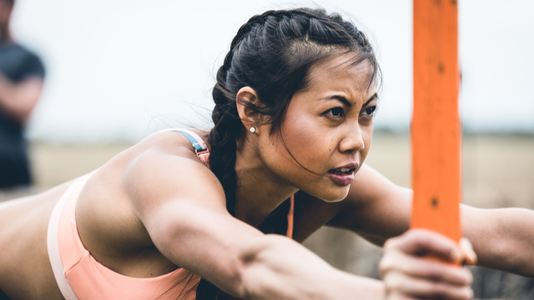 A person wears a sports bra while pushing a loaded sled.