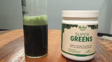 A glass and container of Nested Naturals Super Greens Review