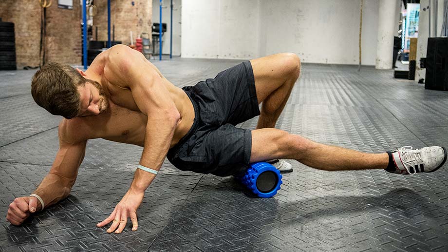 Man in shorts and no t-shirt, rolling his quads on a blue foam roller.