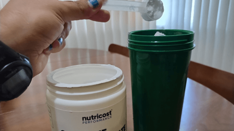 Dumping a scoop of Nutricost Creatine Monohydrate into a shaker cup.