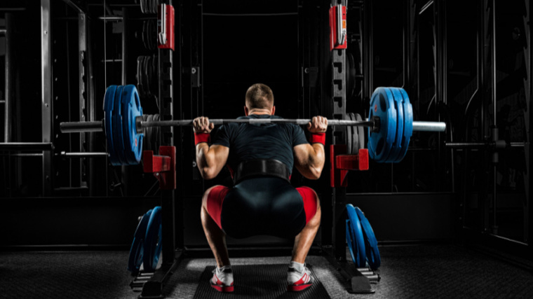 A person faces away from the camera while performing a low bar back squat.