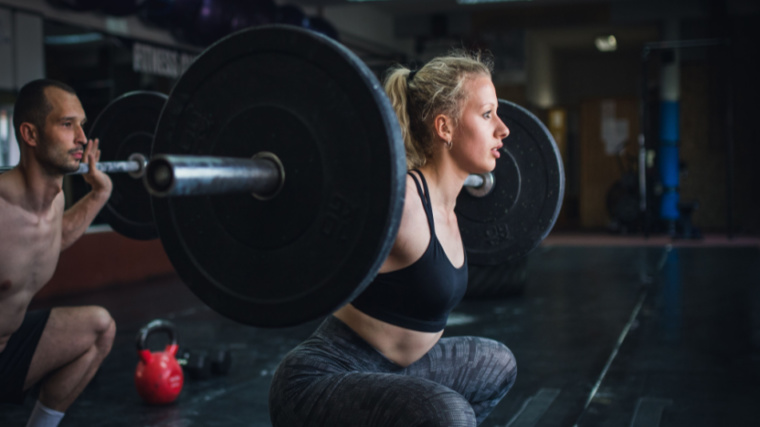 A person wearing a sports bra performs a back squat with a loaded barbell.