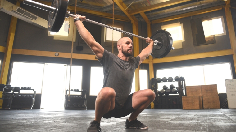 A Middle-Eastern person doing an overhead squat position.