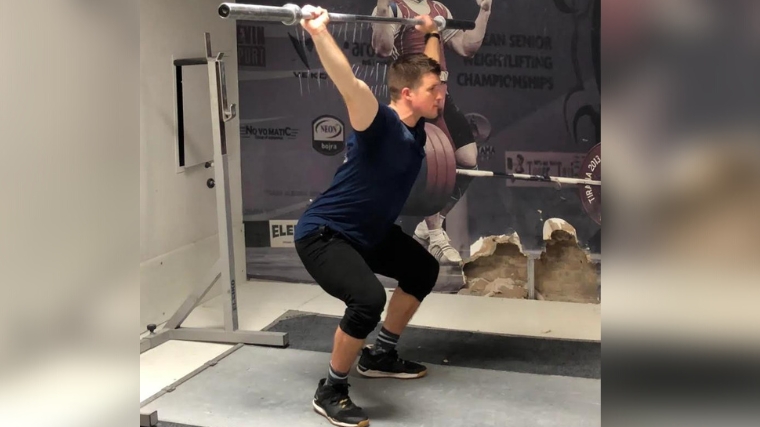 A person establishing position for an overhead squat, with the bar over the back of the neck.