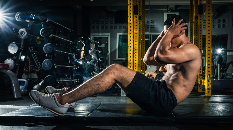 man performs sit-up in dark gym