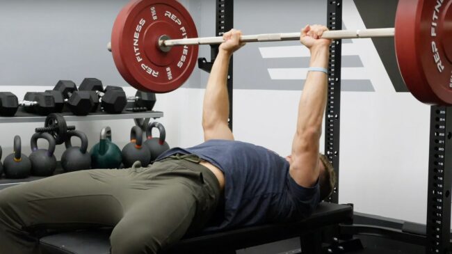 A person performing close-grip bench press, with the barbell all the way up.