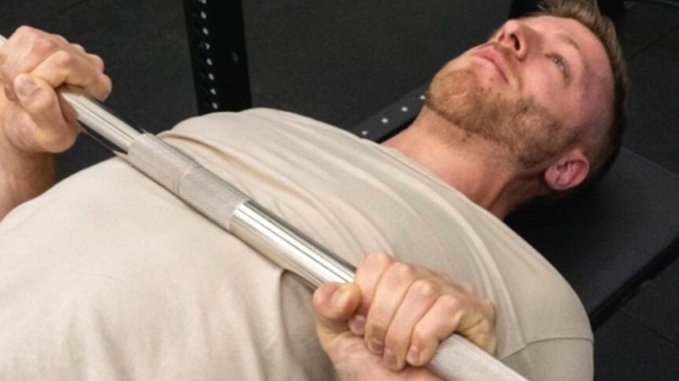 A person holding a barbell in the second position for a bench press.