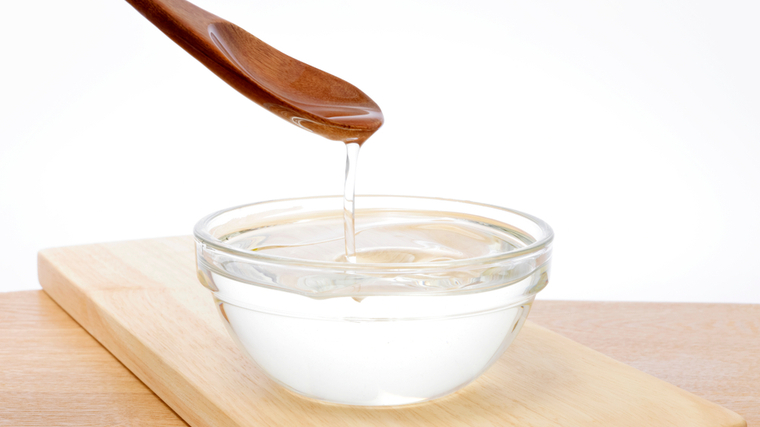 A wooden spoon drips coconut oil over a small clear bowl.