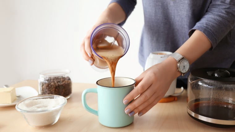 A person transfers coffee from a glass to a teal mug.