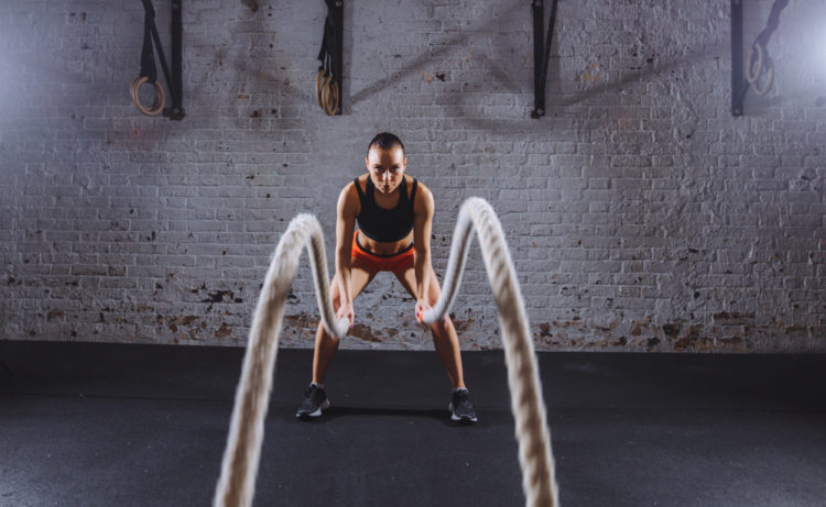 Battle rope, fitness and woman in studio for exercise, strength training  and cardio workout burning calories. Wellness, focus and healthy girl in a  squat pose moving ropes with a blue background Photos