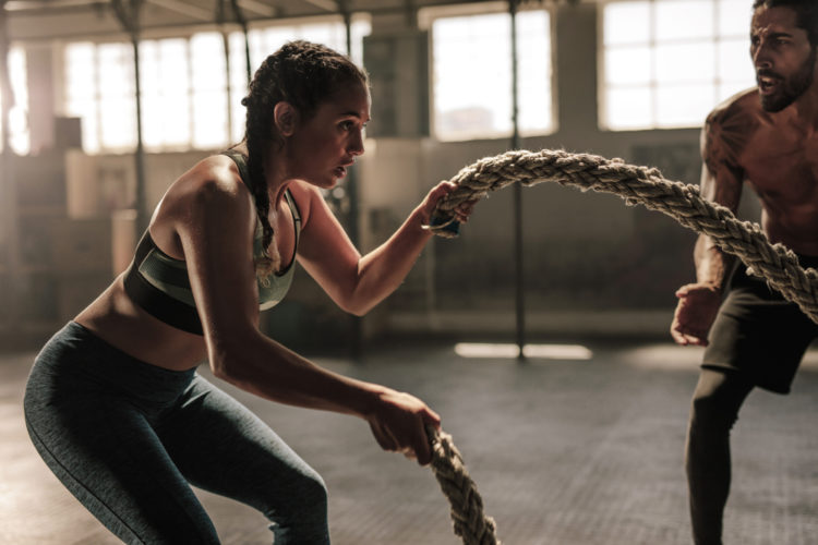 Battle rope, fitness and woman in studio for exercise, strength training  and cardio workout burning calories. Wellness, focus and healthy girl in a  squat pose moving ropes with a blue background Photos