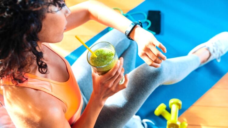 A person looking at their fitness app with a glass of green juice in one hand.