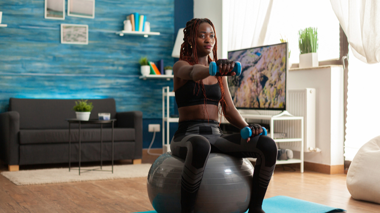 A person performs front raises on a stability ball indoors and at home