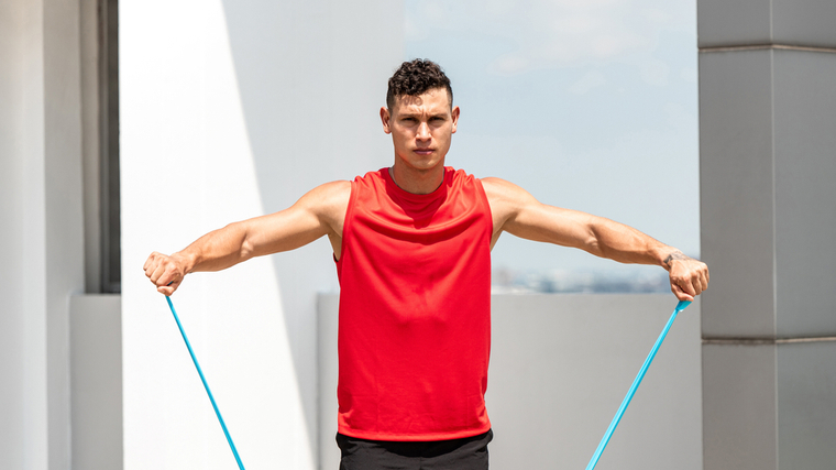 A person performs resistance band lateral raises outside.