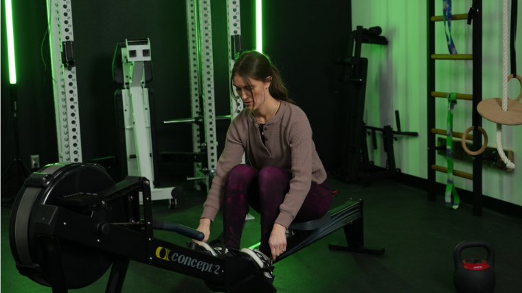 A BarBend tester strapping their feet in the Concept2 RowErg.