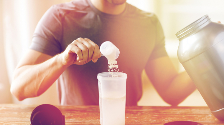 Man scooping mass gainer into shaker bottle