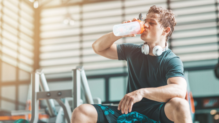 Young man drinking from shaker cup on a weight bench