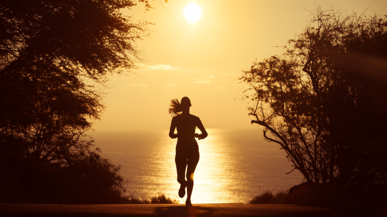 Woman silhouette running on road with sun low in the sky 