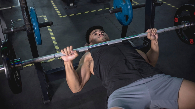 A person wears a black tank top and holds a bench press at the bottom of the lift.