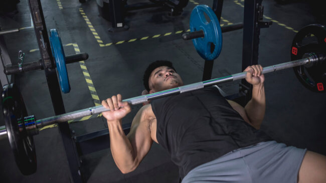 A person wears a black tank top and holds a bench press at the bottom of the lift.