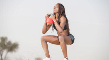 A person performs a kettlebell goblet squat on a beach.