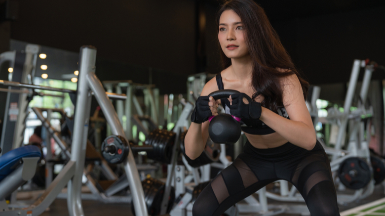 A person performs a kettlebell goblet squat in the gym.