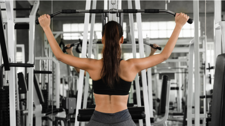 A person faces away from the camera as they set up to perform a lat pulldown.