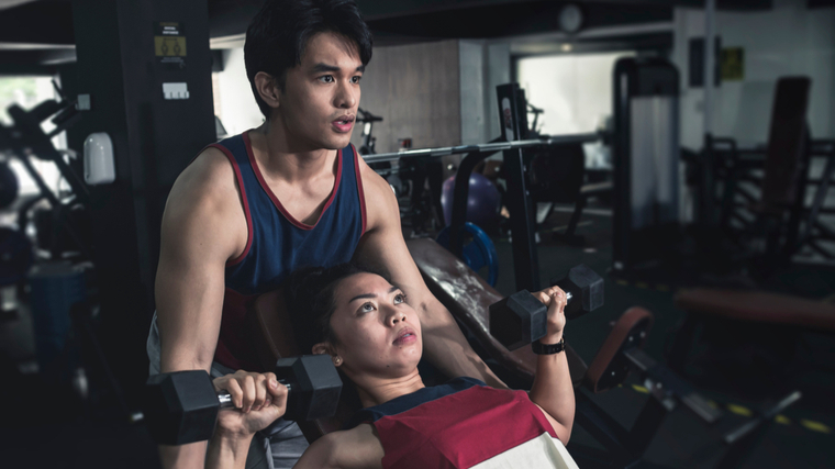 One lifter spots another during an incline dumbbell bench press.