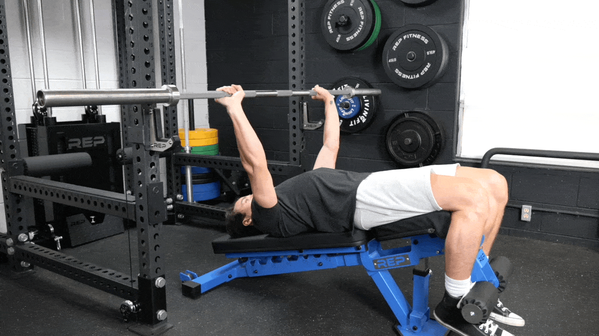 A man lays back-first on a decline bench with his feet secure. He performs barbell bench presses.