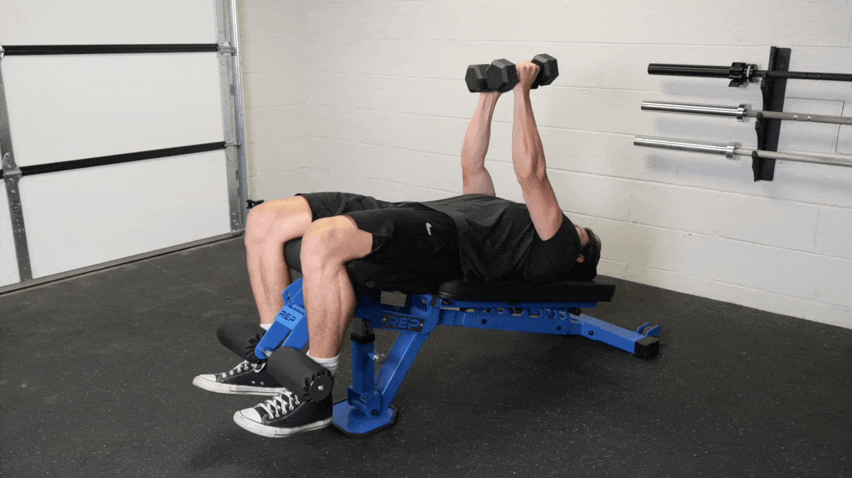 Person in a grey t-shirt and black shorts performs dumbbells flyes on a blue decline bench.