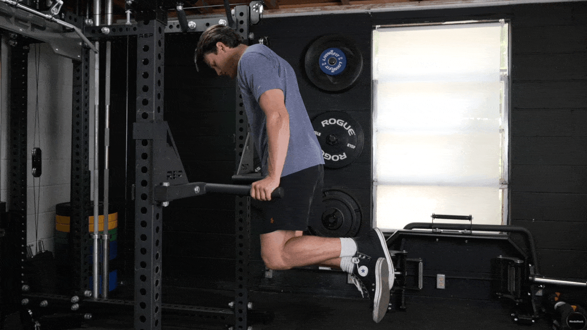 Person ina. grey t-shirt and black shorts performs dips on a horned-shaped implement, attached to a power rack.