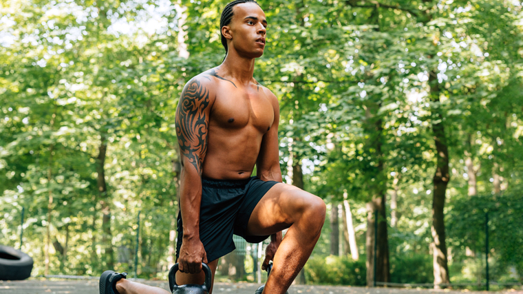 A person performs kettlebell lunges in a park.