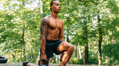 A person performs kettlebell lunges in a park.