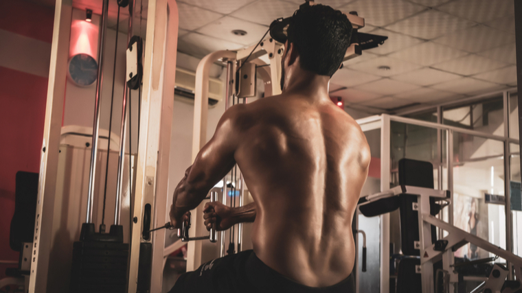 A shirtless person sets up for a seated cable row in the gym.