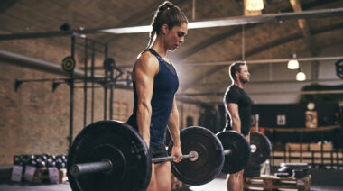 Two people perform deadlifts in the gym.