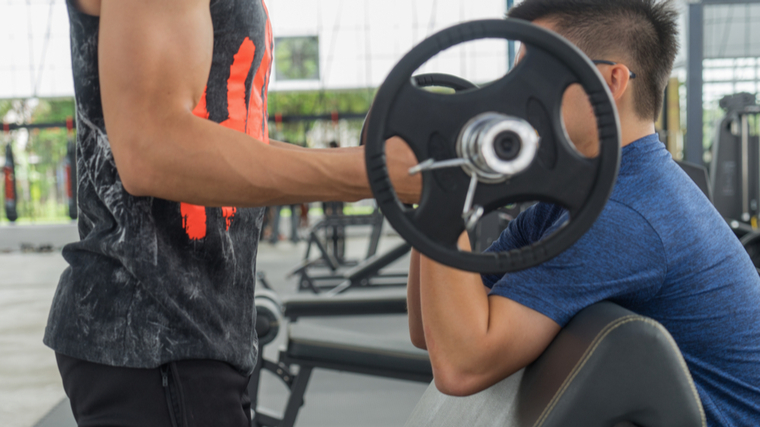 A person performs a forced rep with the help of a spotter in the gym.